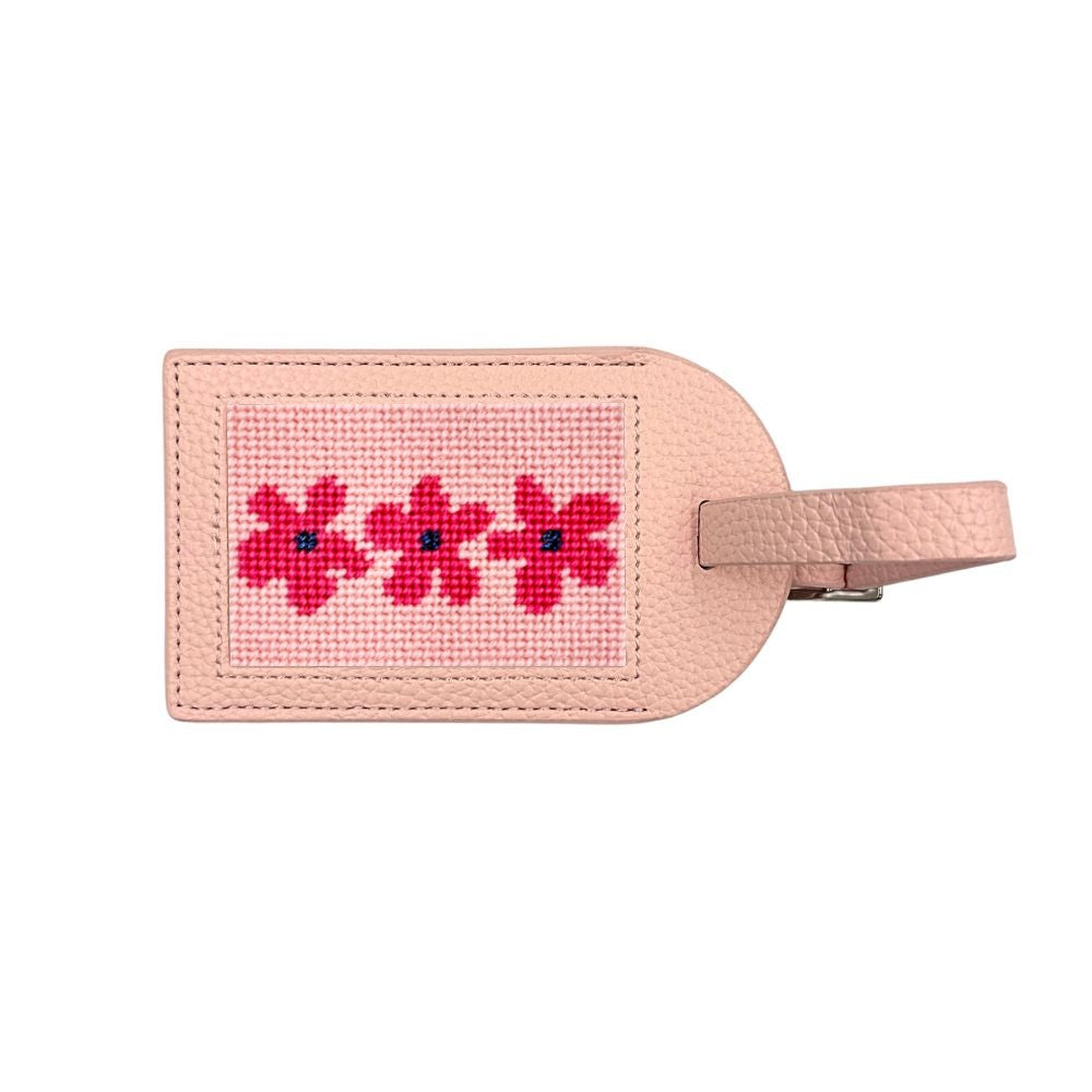 A light pink leather luggage tag featuring a rectangular canvas insert with three embroidered red flowers with blue centers, and a matching leather loop on the right.