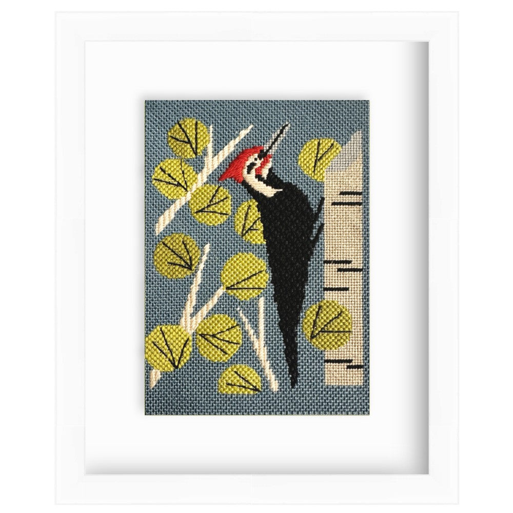 Framed artwork of a woodpecker on a branch with leaves and a tree trunk.