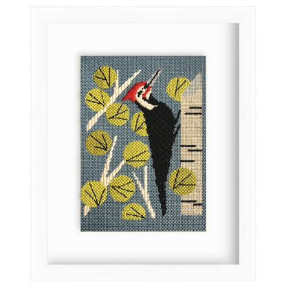 Framed artwork of a woodpecker on a branch with leaves and a tree trunk.