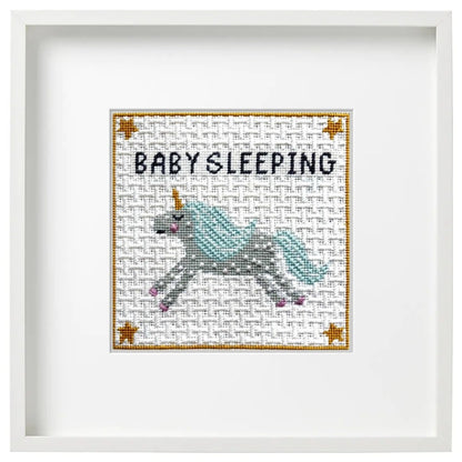 Baby sleeping needlepoint kit design shown in a white frame.